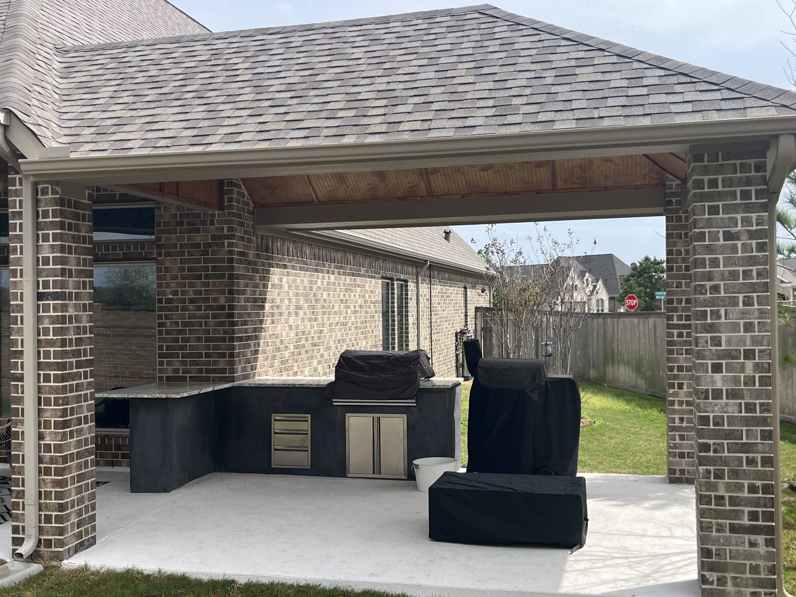 Shingle-roof patio cover with brick columns over an outdoor kitchen