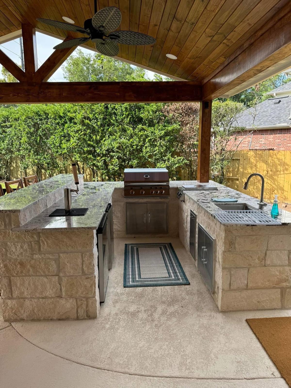 Stone outdoor kitchen with granite countertops under a cedar-beam patio cover