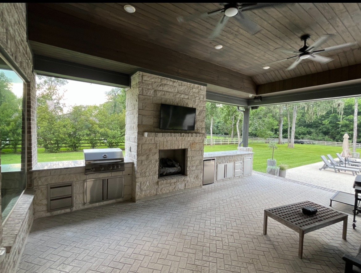 Covered patio with a stone fireplace, TV and built-in outdoor kitchen
